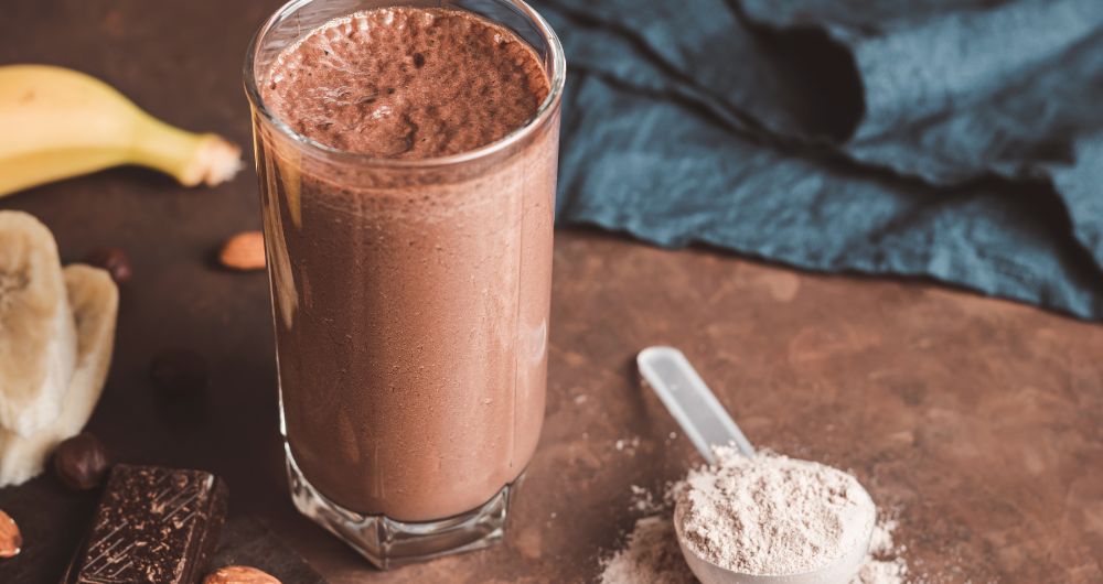 Chocolate protein shake with protein powder scoop on a table
