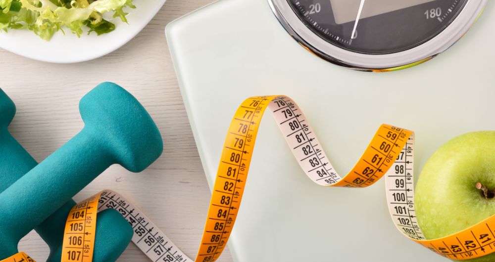 Dumbbells, measuring tape, scale, apple, and healthy food representing fitness, weight loss, and healthy living.