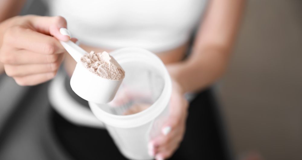 Person scooping protein powder into a shaker bottle
